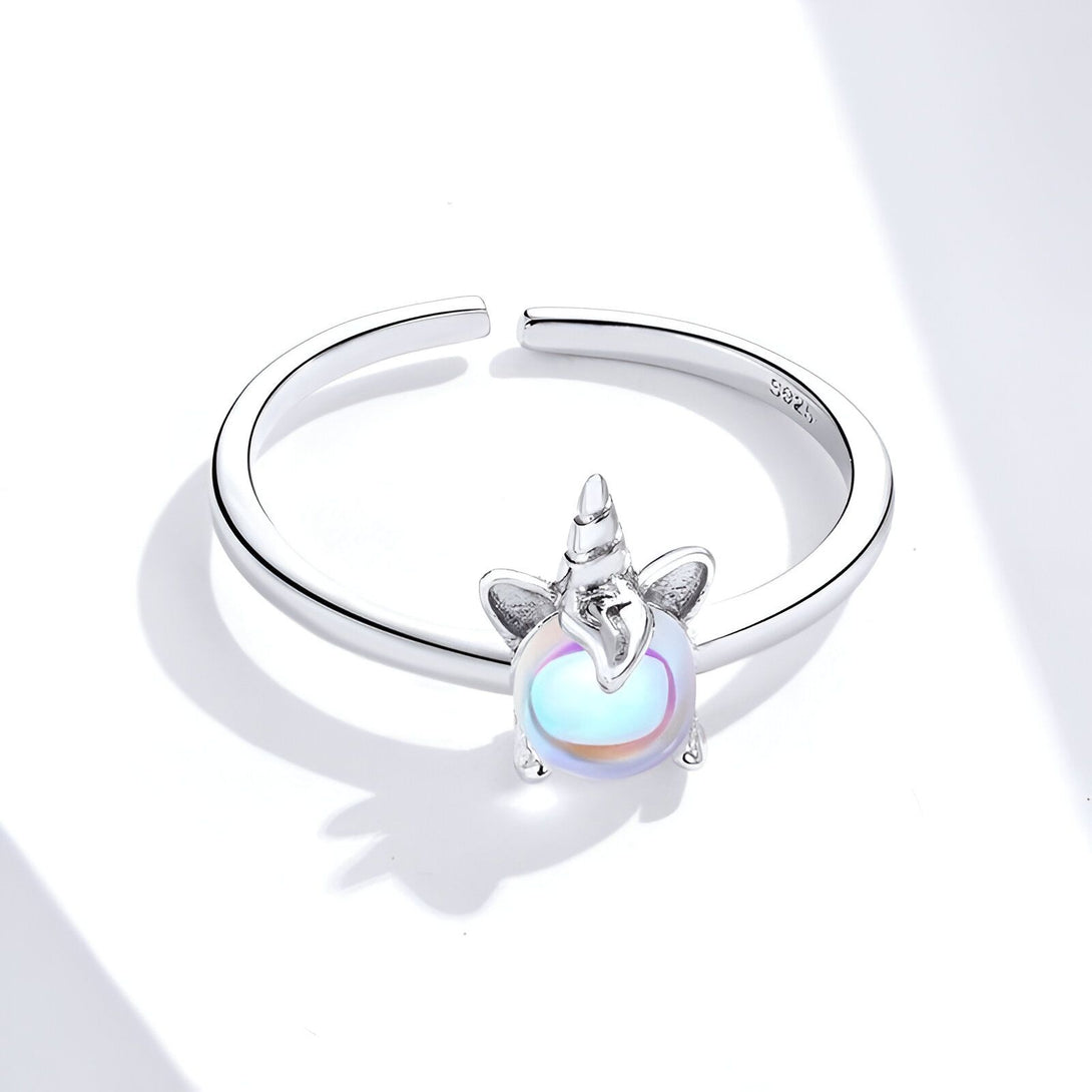 Une bague en argent avec une pierre précieuse en forme de licorne. La pierre précieuse est de couleur arc-en-ciel et a une forme de dôme. La bague est en argent sterling 925 et est ajustable.