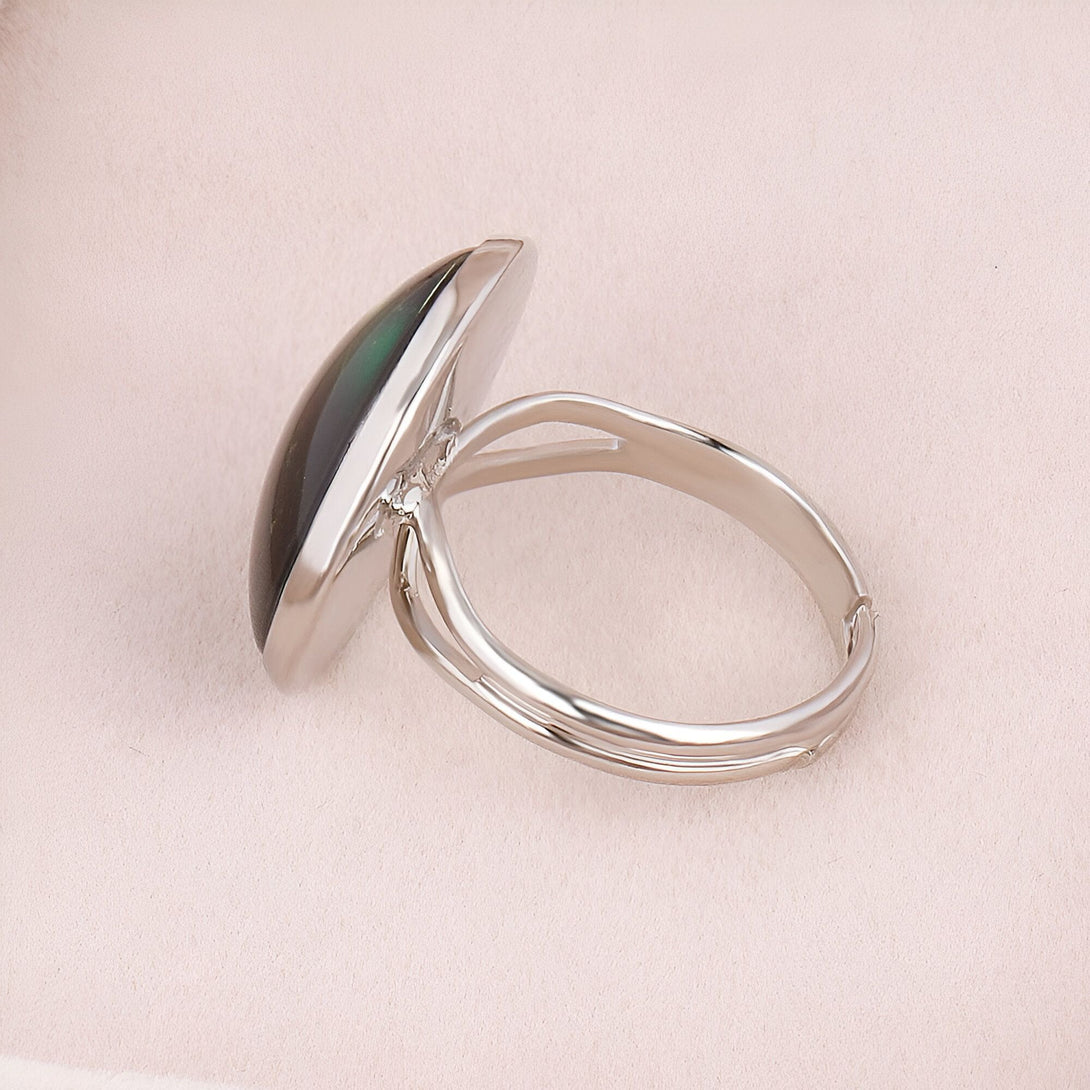 Une bague en argent avec une pierre ovale verte sertie au centre. La bague est vue de côté.