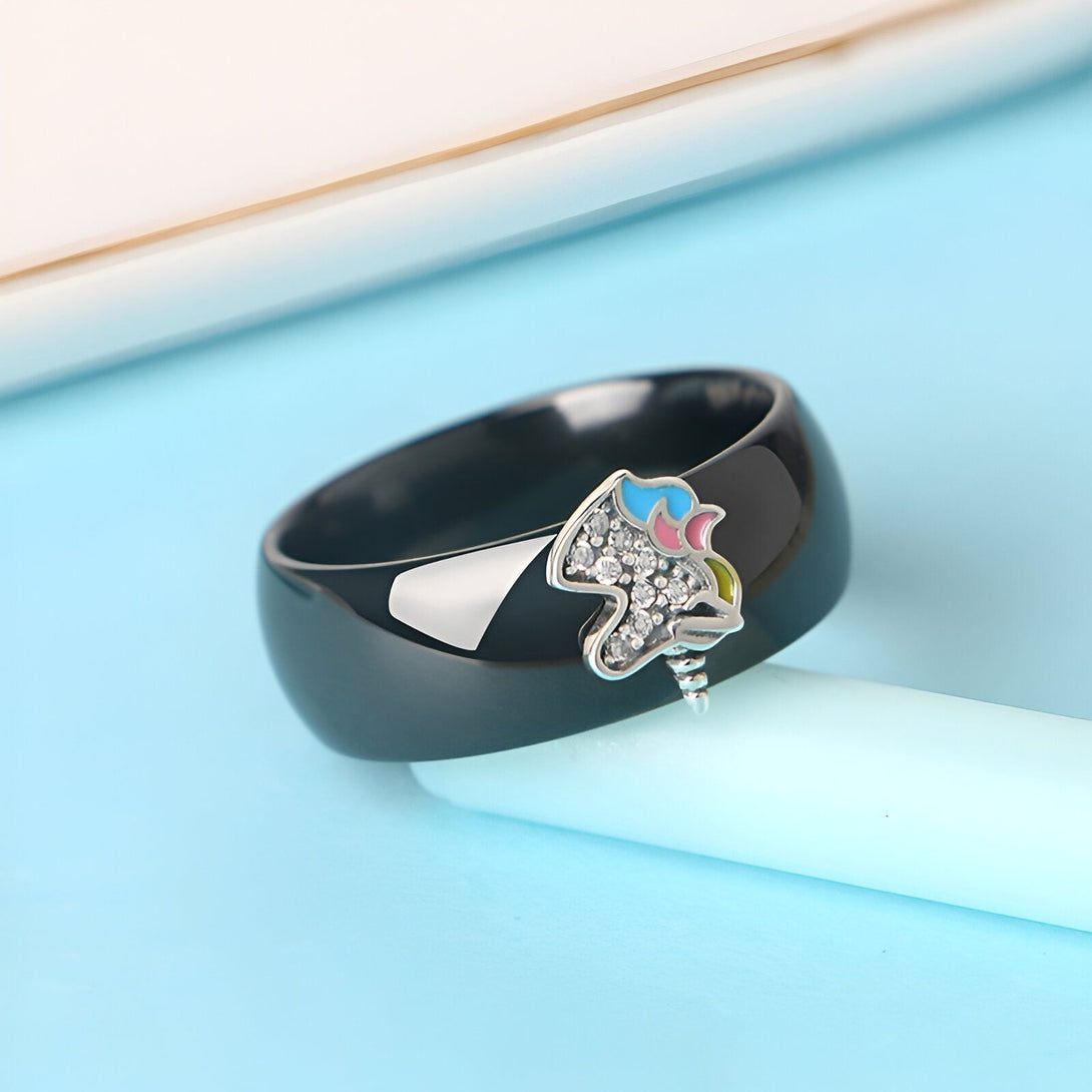 Bague en céramique noire avec une licorne incrustée. La licorne est colorée avec des émaux de couleur rose, bleu et jaune et a une corne en argent.