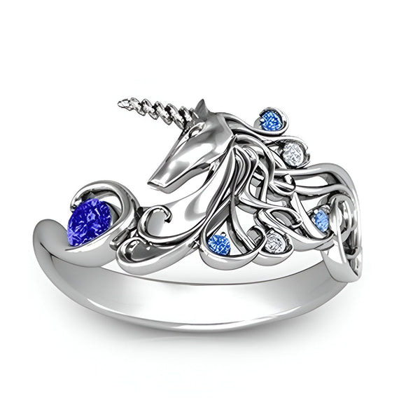 Une bague en argent avec une pierre précieuse bleue et des cristaux blancs et bleus. La bague est en forme de licorne.