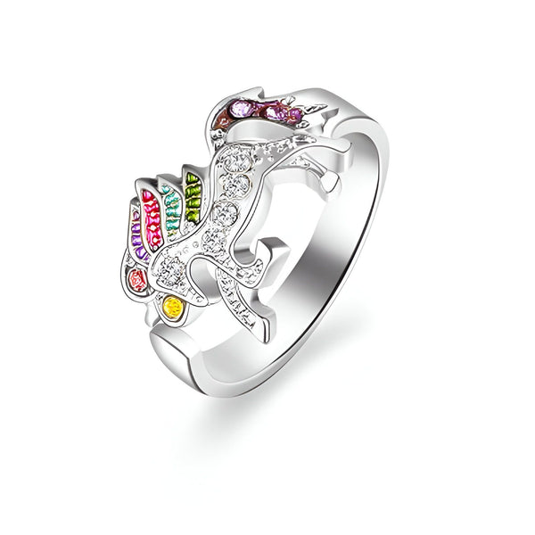  L'image montre une bague en forme de licorne. La licorne est sertie de cristaux de différentes couleurs. La bague est en argent.