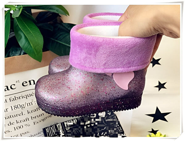 Gros plan d'une botte de pluie pour enfant, pailletée et violette, avec une doublure en fausse fourrure blanche. Une main tient la botte ouverte. Décor de feuilles vertes et emballage cadeau en arrière-plan. Idéales pour les jours de pluie !, 45501103014143,45501103046911,45501103079679,45501103112447,45501103145215,45501103177983,45501103210751,45501103243519,45501103276287 | Licorne Shop