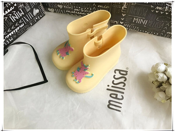 Paire de bottes de pluie jaunes Mini Melissa pour enfants, avec un motif de cheval rose et bleu. Elles sont sur un tissu blanc à côté de leur boîte., 45501099376895,45501099409663,45501099442431,45501099475199,45501099507967,45501099540735,45501099573503,45501099606271,45501099639039 | Licorne Shop