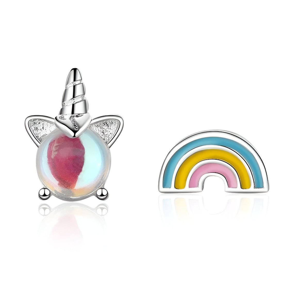 Une image de deux boucles d'oreilles en forme de licorne et d'arc-en-ciel. Les boucles d'oreilles sont en argent et l'arc-en-ciel est coloré.