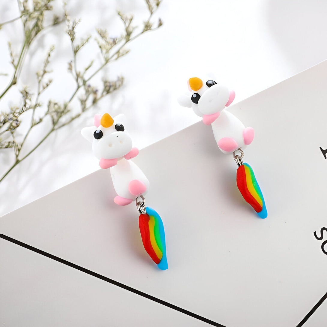 Une paire de boucles d'oreilles en forme de licorne blanche avec une crinière et une queue arc-en-ciel.