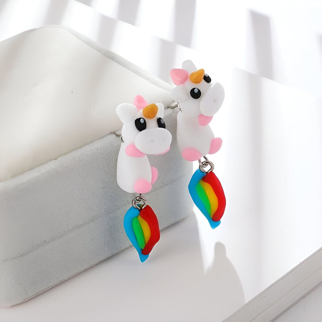 Une paire de boucles d'oreilles en forme de licorne blanche avec une crinière et une queue arc-en-ciel.