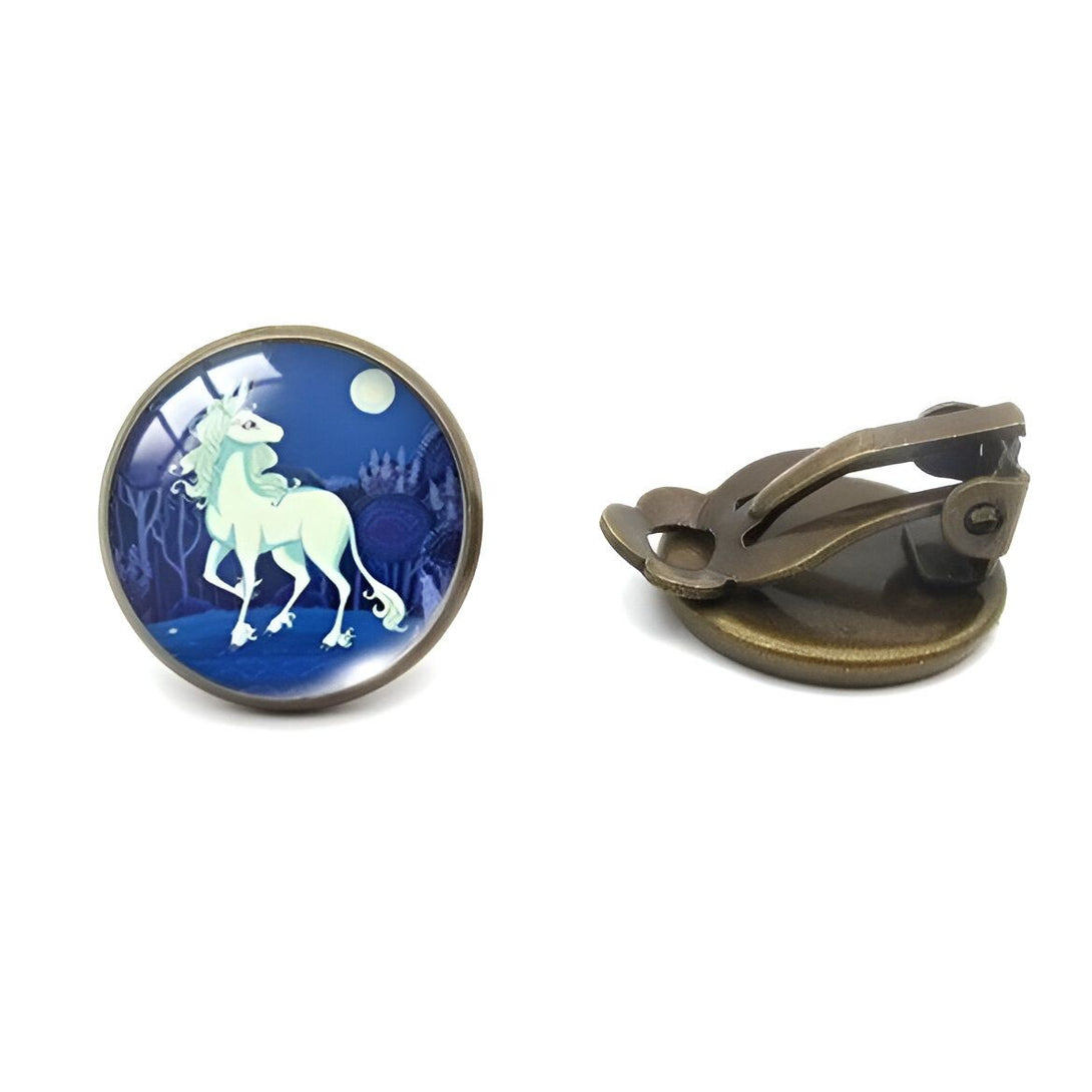 Une paire de boucles d'oreilles en bronze avec un cabochon en verre rond représentant une illustration d'une licorne blanche marchant dans une forêt la nuit.