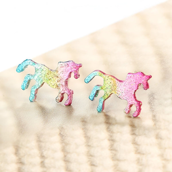 Une paire de boucles d'oreilles en forme de licorne. Les licornes sont multicolores et ont des paillettes.