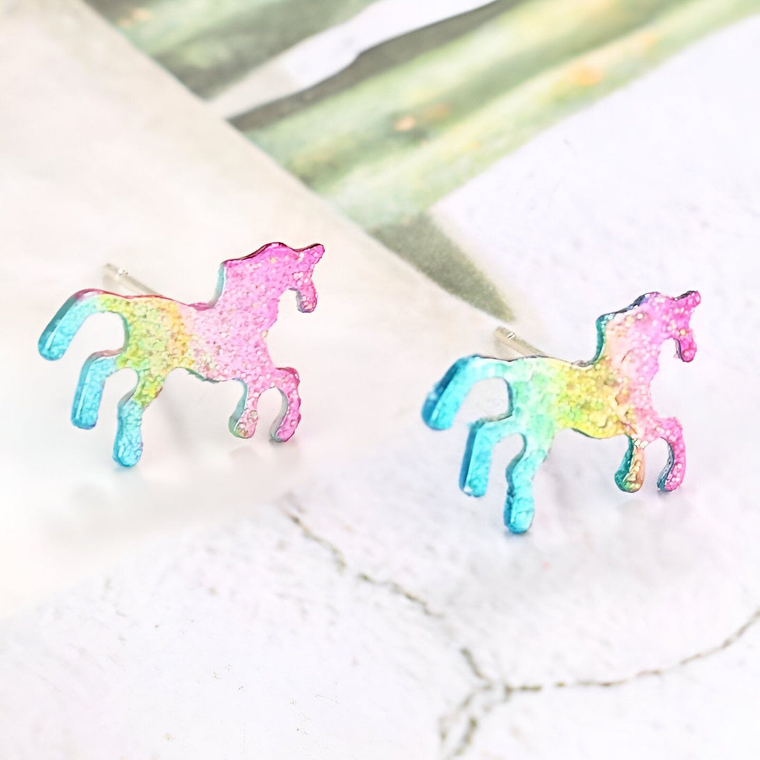 Une paire de boucles d'oreilles en forme de licorne. Les licornes sont colorées avec un dégradé de couleurs arc-en-ciel.