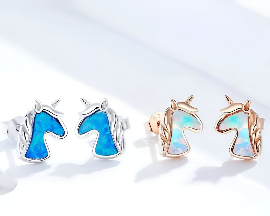 Deux boucles d'oreilles en forme de tête de licorne avec des pierres précieuses bleues et blanches.