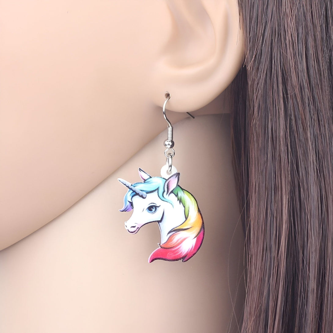 Une image d'une boucle d'oreille en forme de licorne. La licorne est blanche avec une crinière et une queue arc-en-ciel. La boucle d'oreille est en métal argenté.