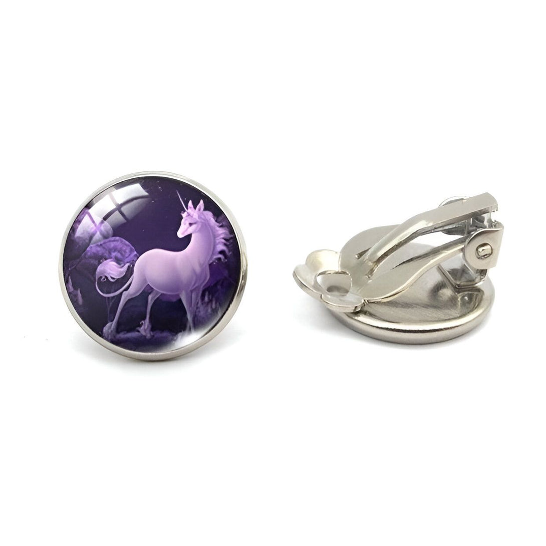 Une paire de boucles d'oreilles en forme de licorne violette. Les boucles d'oreilles sont en métal argenté et ont une forme ronde. La licorne est représentée avec une crinière et une queue roses, et est entourée d'un fond violet. Les boucles d'oreilles sont de type clip.