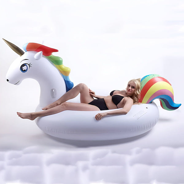 Femme en maillot de bain noir se détendant sur une bouée licorne gonflable blanche avec une crinière et une queue arc-en-ciel. Style de vie estival, amusement à la piscine, détente et insouciance., 45501243949311 | Licorne Shop