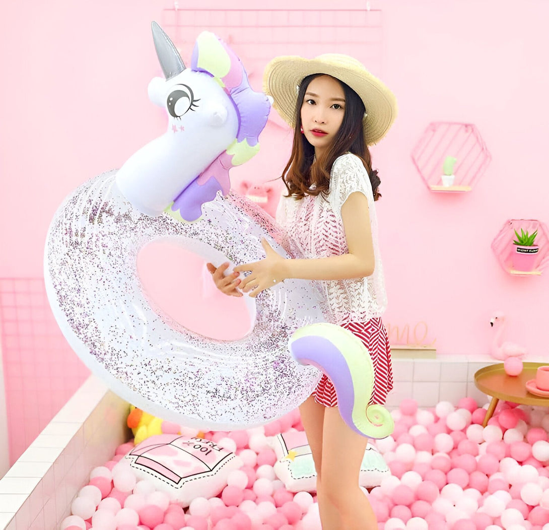 Une jeune femme en chapeau de paille tient une bouée gonflable licorne scintillante dans un décor rose pastel avec des balles roses et blanches., 45501244244223 | Licorne Shop