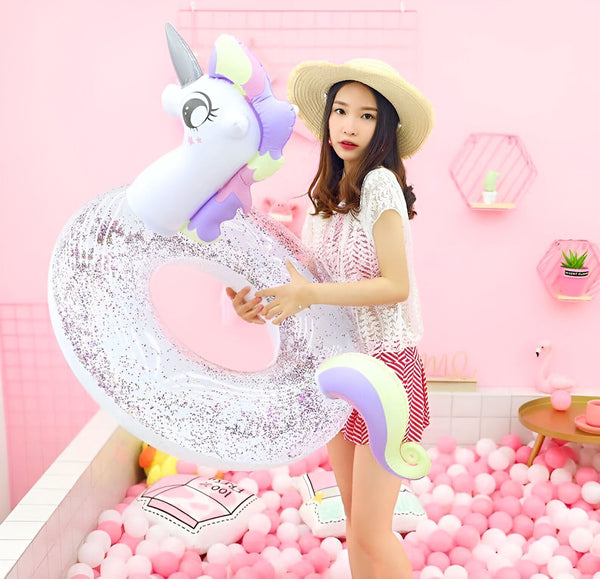 Une jeune femme en chapeau de paille tient une bouée gonflable licorne scintillante dans un décor rose pastel avec des balles roses et blanches., 45501244244223 | Licorne Shop