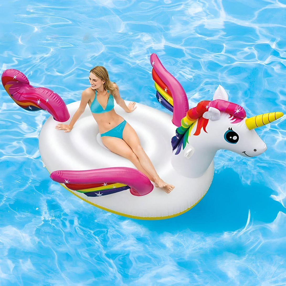 Femme souriante en bikini bleu turquoise flottant sur une bouée gonflable licorne blanche dans une piscine d'eau bleue. La licorne a des ailes roses avec des rayures arc-en-ciel, une corne jaune et une crinière multicolore., 45501244932351 | Licorne Shop