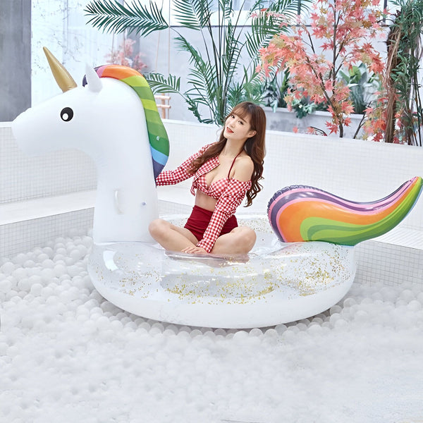 Jeune femme en maillot de bain rouge assise sur une bouée licorne gonflable dans une piscine à balles blanches. Décoration tropicale en arrière-plan., 45501227892991 | Licorne Shop