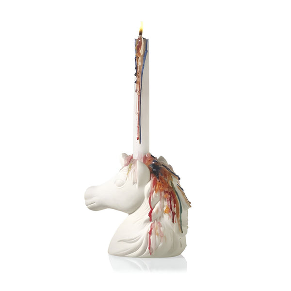 Photographie d'un bougeoir unique en forme de tête de licorne blanche. Une chandelle brûle sur le dessus, avec de la cire colorée qui coule, ajoutant une touche artistique et originale. Décoration intérieure tendance et fantaisiste., 45501142991103 | Licorne Shop