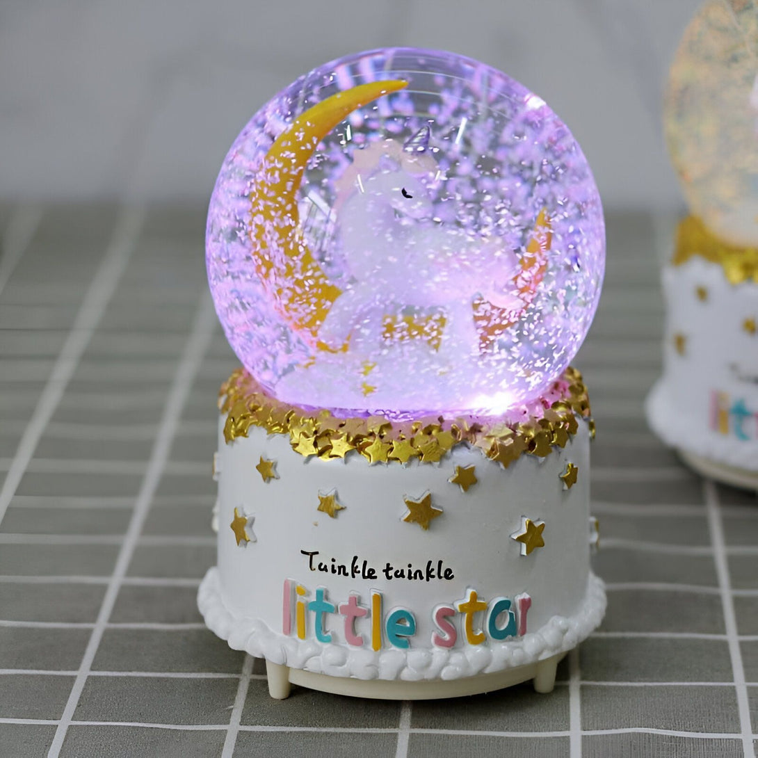 Boule à neige musicale avec licorne et lune dorée. La base blanche décorée d'étoiles dorées porte l'inscription "Twinkle twinkle little star". Éclairage intérieur violet. Décoration féérique pour chambre d'enfant., 45501133553919 | Licorne Shop