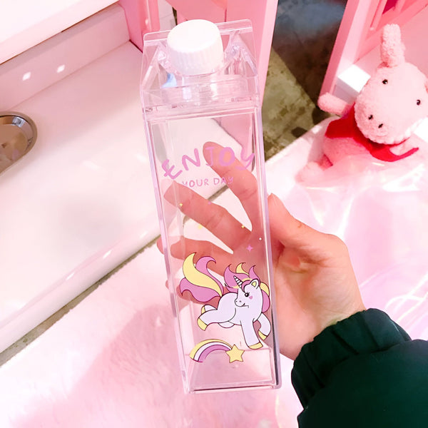 Bouteille d'eau transparente en forme de carton de lait avec un dessin de licorne. Une main la tient. Le décor est rose, avec une peluche et un meuble., 45501175824639 | Licorne Shop