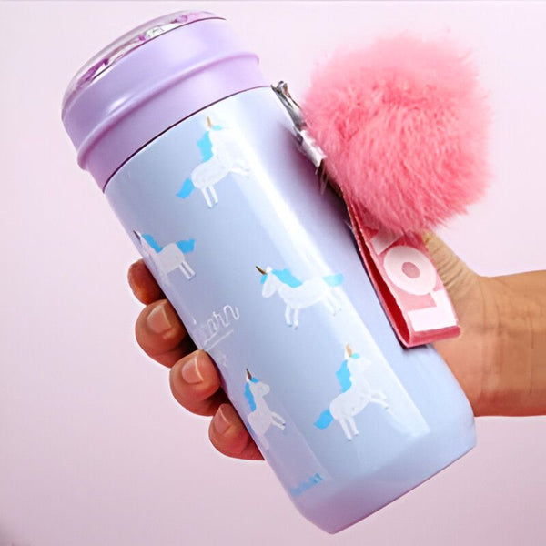 Bouteille d'eau pastel avec des motifs de licornes et un pompon rose. Couvercle violet et sangle de transport blanche et rouge. Main tenant la bouteille., 45501177069823 | Licorne Shop