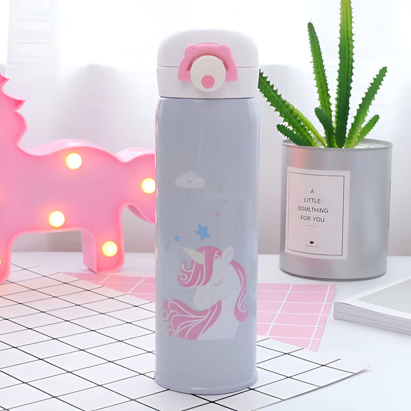 Gourde thermos décorée d'un motif de licorne rose et blanche sur fond gris, avec un bouchon blanc orné d'une fleur rose. Un cactus et une veilleuse licorne rose sont visibles en arrière-plan., 45501178249471 | Licorne Shop
