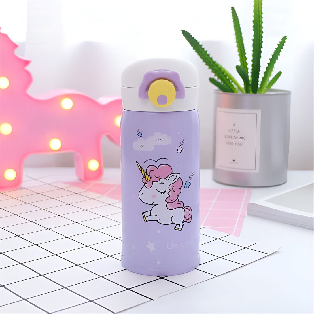 Thermos violet avec un dessin de licorne, posé sur une surface à carreaux. En arrière-plan, une licorne rose lumineuse et une plante verte., 45501174022399 | Licorne Shop