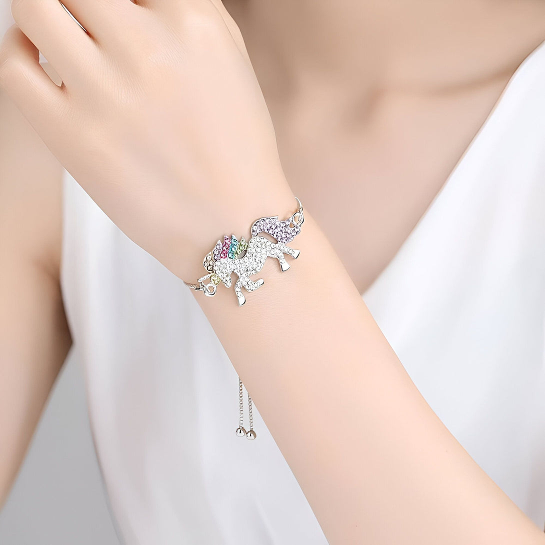 L'image montre un bracelet en argent avec un pendentif licorne. La licorne est sertie de cristaux multicolores. Le bracelet est porté par une femme.