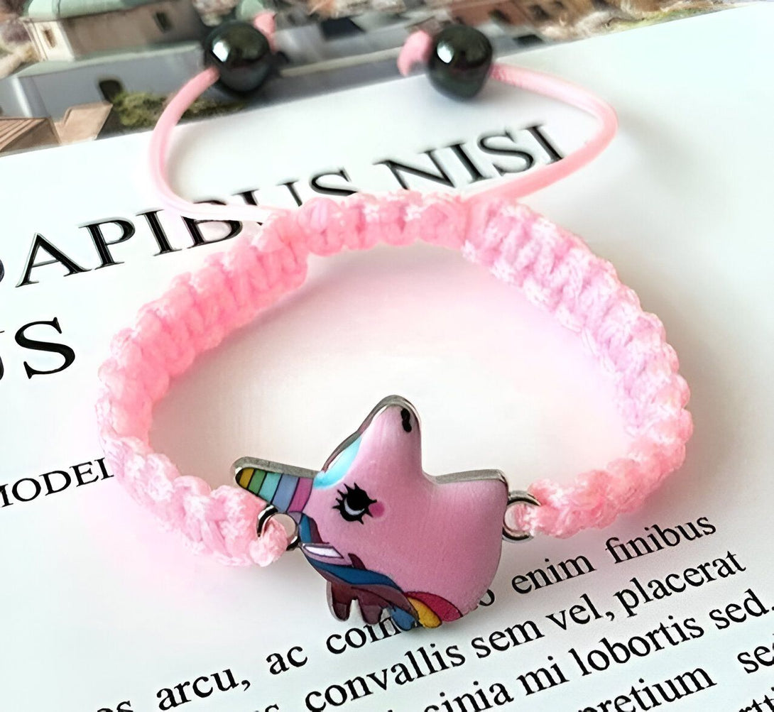 Un bracelet rose avec un pendentif licorne en émail. La licorne est rose avec une crinière et une queue arc-en-ciel. Le bracelet est fait de corde tressée rose.