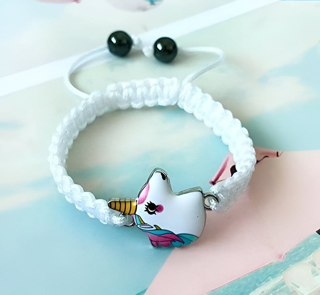 Un bracelet en corde blanche avec un pendentif licorne en métal émaillé. La licorne est blanche avec une crinière et une queue arc-en-ciel.