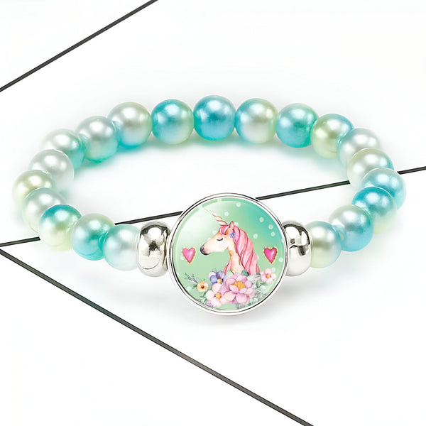 Bracelet de perles turquoise avec un pendentif rond argenté orné d'une illustration d'une licorne aux cheveux roses entourée de fleurs et de coeurs. Bijou fantaisie pour enfant., 45501396615423 | Licorne Shop