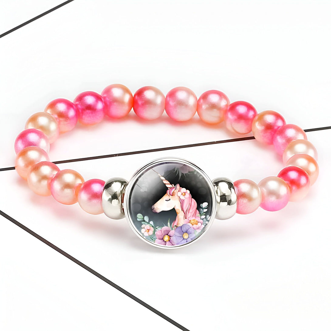 Bracelet de perles roses avec un médaillon licorne. Bijou fantaisie pour enfant avec un pendentif représentant une licorne entourée de fleurs., 45501422600447 | Licorne Shop