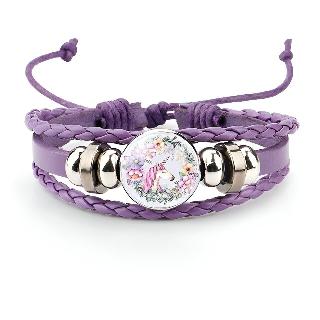 Le bracelet en cuir tressé de couleur mauve comporte un médaillon rond en verre avec une image de licorne blanche avec une crinière et une queue roses et des fleurs colorées tout autour.