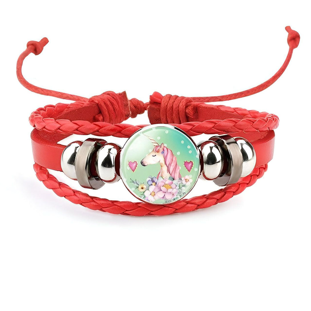 Un bracelet en cuir rouge avec un pendentif en verre rond. Le pendentif représente une licorne blanche avec une crinière et une queue roses. La licorne est entourée de fleurs et de coeurs.