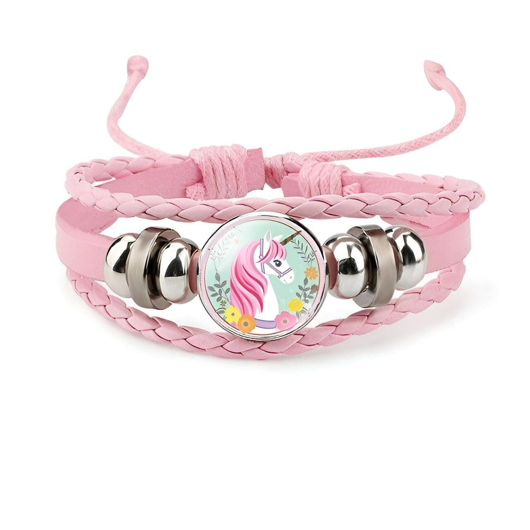 Un bracelet en cuir rose avec un pendentif en verre rond qui représente une licorne blanche avec une crinière et une queue roses. La licorne est entourée de fleurs et de feuilles vertes.