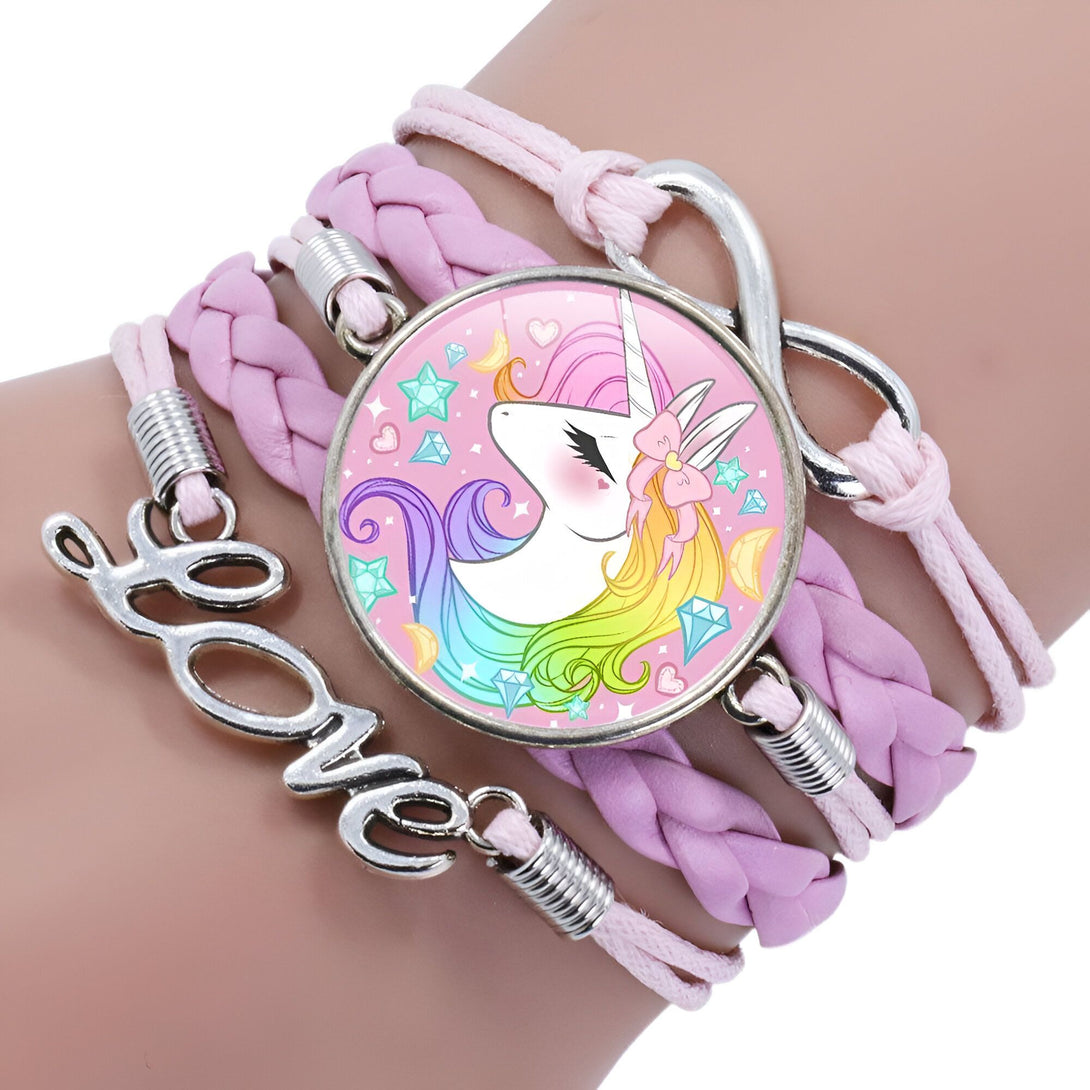 Le bracelet est en cuir tressé rose avec un fermoir en forme d'infini. Il y a un médaillon rond en verre avec une image d'une licorne blanche avec une crinière et une queue arc-en-ciel. La licorne a une fleur rose dans les cheveux et est entourée de coeurs et d'étoiles. Il y a aussi le mot "love" en métal argenté sur le bracelet.