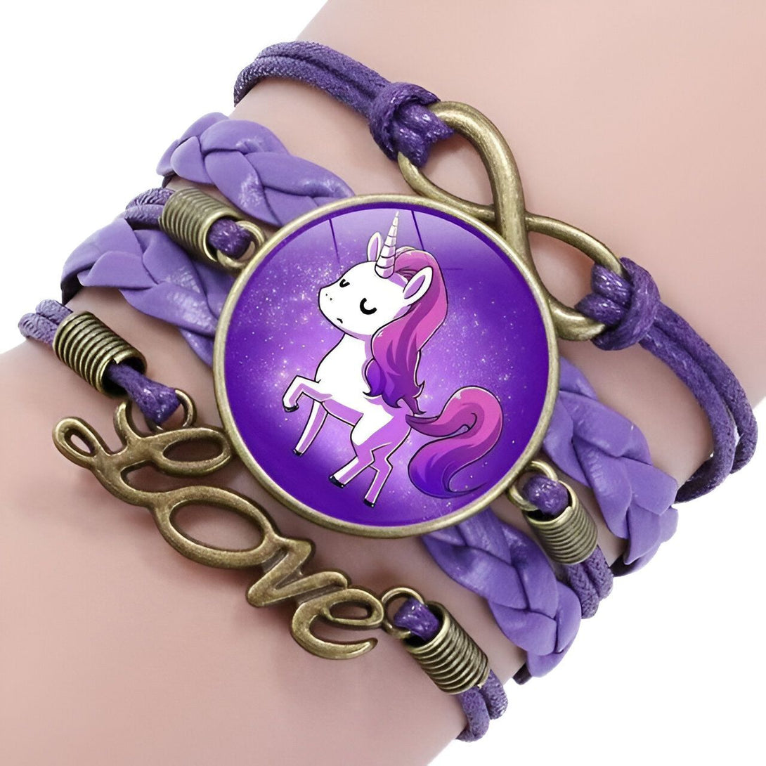 Un bracelet en cuir tressé de couleur mauve avec un pendentif en forme de licorne. La licorne est représentée avec une crinière et une queue violettes, et elle se tient debout sur un fond étoilé. Le bracelet est également orné d'un charm en forme de cœur avec le mot "love" écrit dessus.