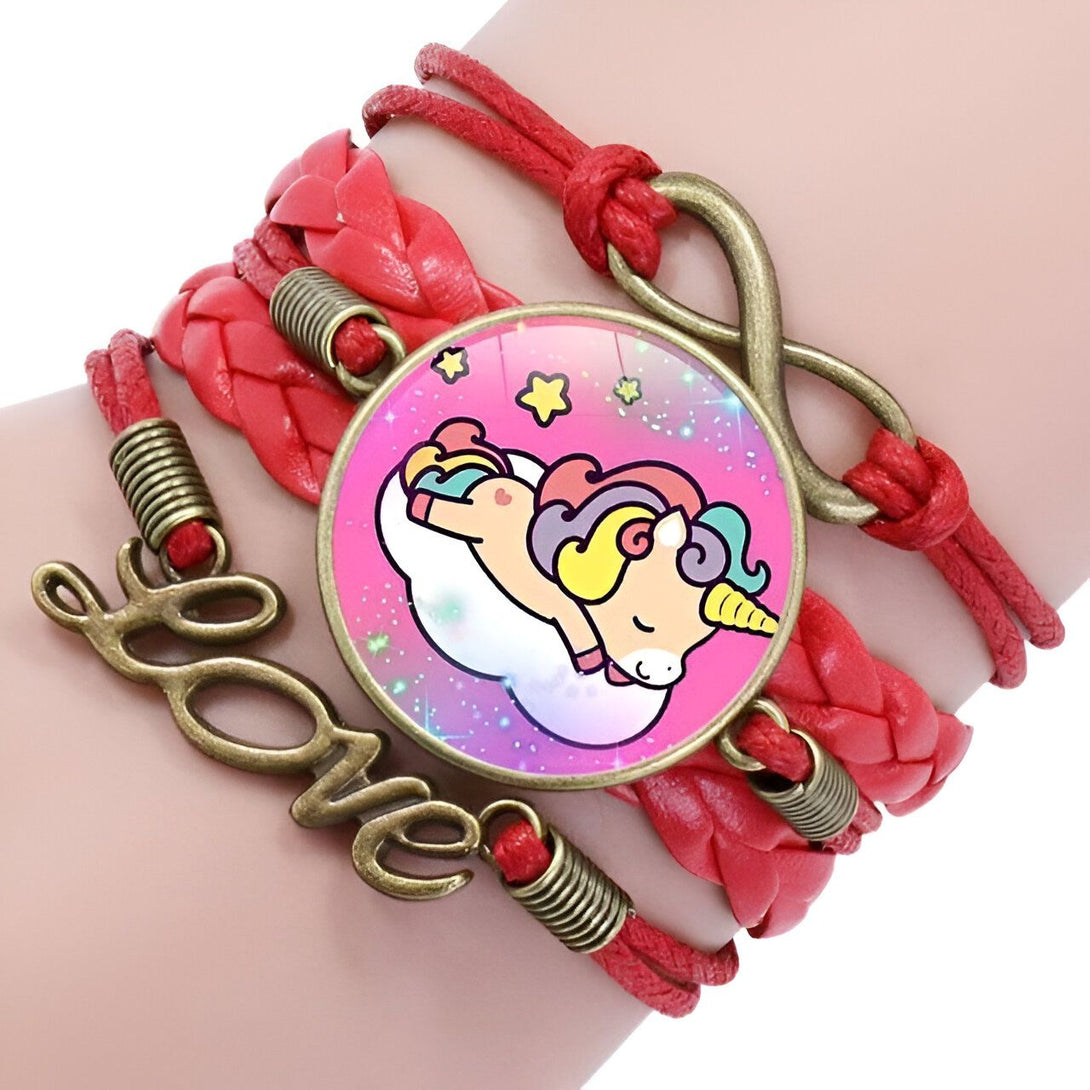 L'image montre un bracelet en cuir rouge avec un pendentif en forme de licorne endormie sur un nuage. Le bracelet est également décoré de deux breloques en forme de cœur et d'une breloque en forme d'infini.