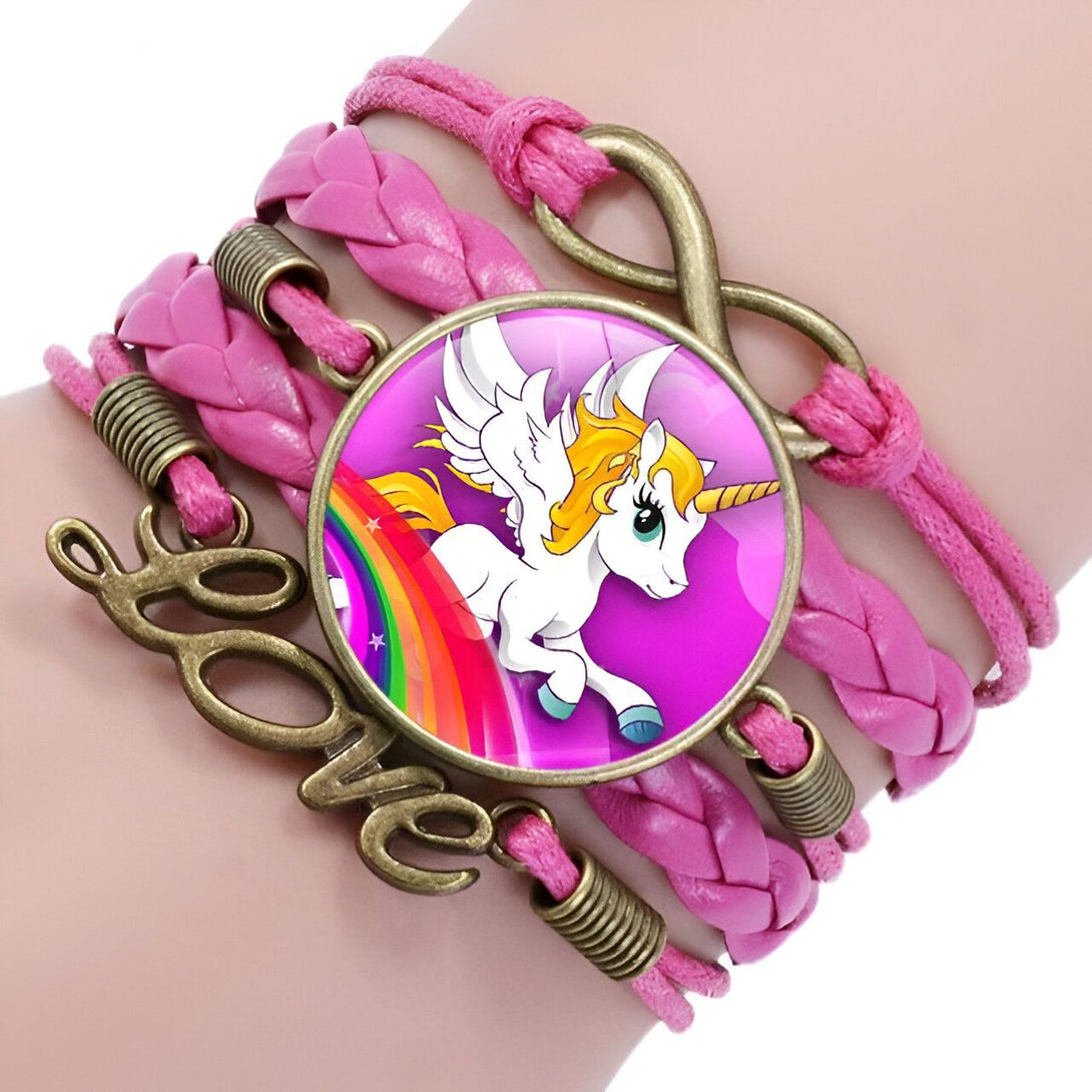 Il s'agit d'un bracelet en cuir rose avec un fermoir en forme de signe de l'infini. Le bracelet est décoré d'un médaillon en verre rond avec une image d'une licorne ailée blanche et jaune sur un fond rose avec un arc-en-ciel. Le mot "love" est écrit en lettres métalliques sur le côté du bracelet.