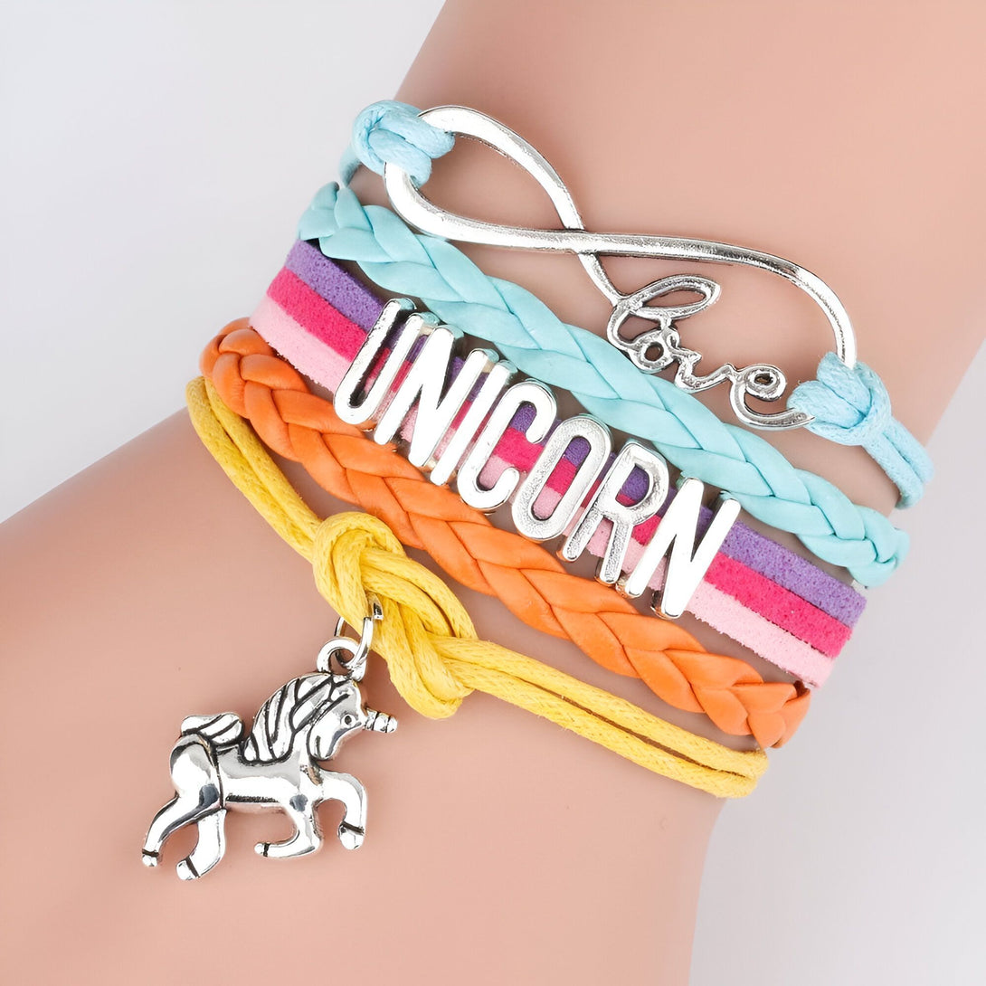 L'image montre un bracelet en cuir avec un pendentif licorne. Le bracelet est composé de plusieurs lanières de couleurs différentes, avec le mot "UNICORN" écrit sur l'une d'elles. Le pendentif est en métal argenté et représente une licorne.