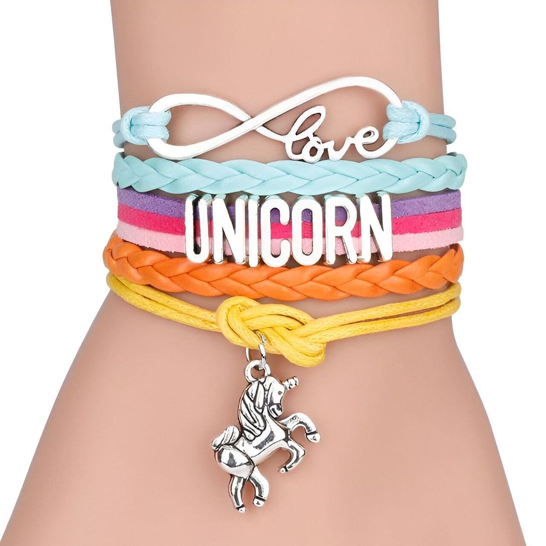 L'image montre un bracelet en cuir avec un pendentif en forme de licorne. Le bracelet est composé de quatre brins de cuir de couleurs différentes : bleu clair, rose, orange et jaune. Le pendentif est en métal argenté et représente une licorne.