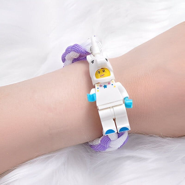 Bracelet tressé violet et blanc avec un personnage LEGO d'astronaute en costume de licorne blanche sur un poignet. Le fond est un tissu blanc et doux., 45501256630527 | Licorne Shop
