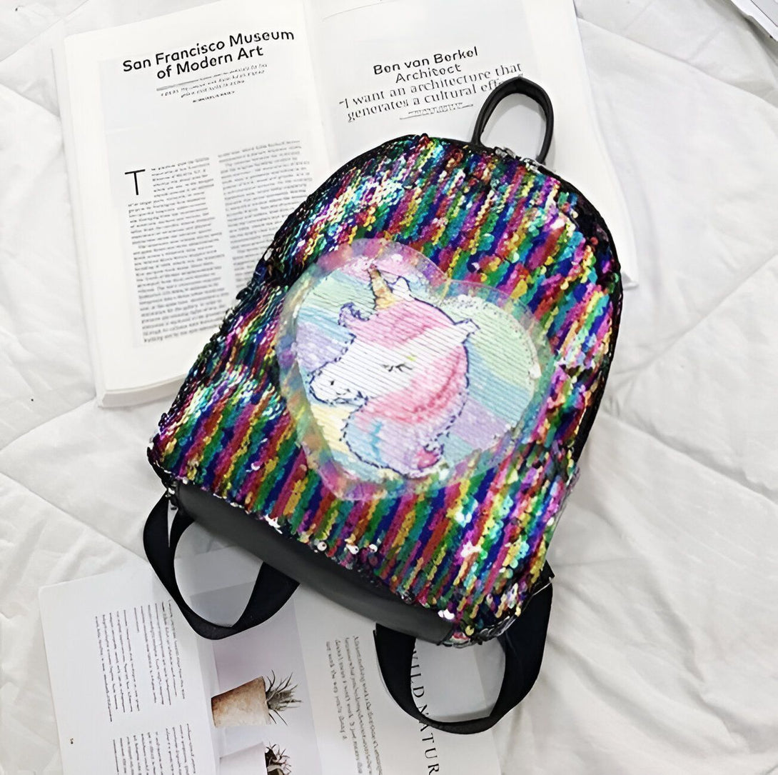 Un sac à dos à paillettes réversibles avec une image de licorne. Les paillettes sont de couleur arc-en-ciel et le sac à dos est noir à l'arrière.