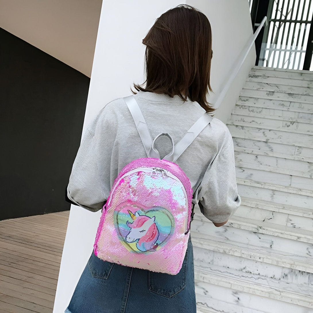 Une jeune fille porte un sac à dos rose à sequins avec une image de licorne.