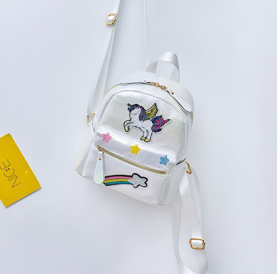 Un sac à dos blanc avec une image de licorne ailée. Il y a aussi des étoiles et un arc-en-ciel sur le sac à dos.