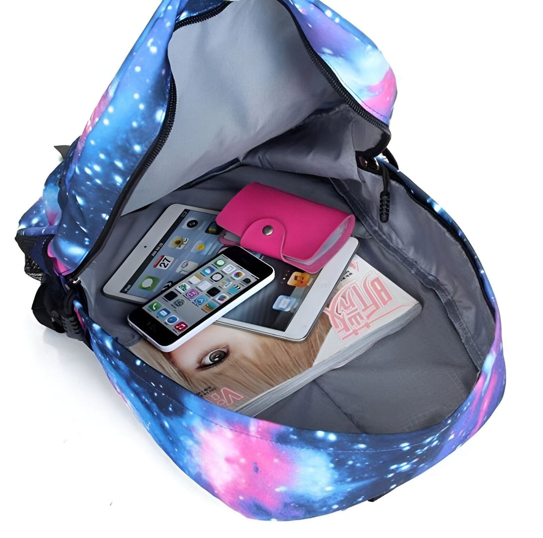 Un sac à dos ouvert avec à l'intérieur un téléphone portable, un portefeuille rose, une tablette et un magazine. Le sac à dos est bleu et violet avec des étoiles.