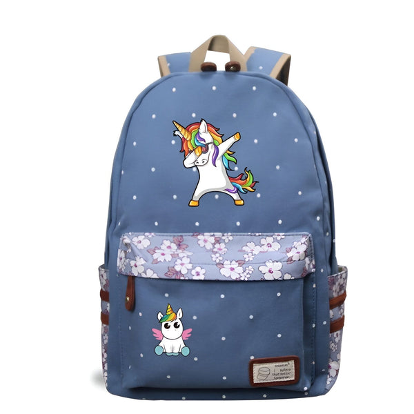 Une image d'un sac à dos bleu avec une image de licorne qui fait le dab. Il y a aussi une petite image de licorne sur la poche avant du sac à dos. Le sac à dos est recouvert de pois blancs et de fleurs roses.