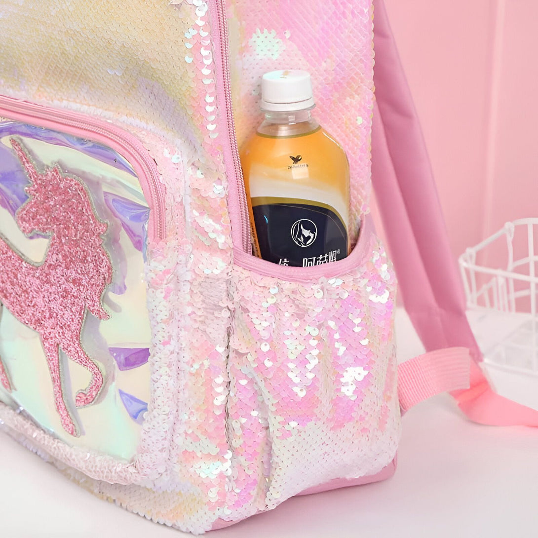 Une image d'un sac à dos rose à paillettes avec une poche latérale en filet contenant une bouteille d'eau. Le sac à dos est décoré d'une image de licorne.