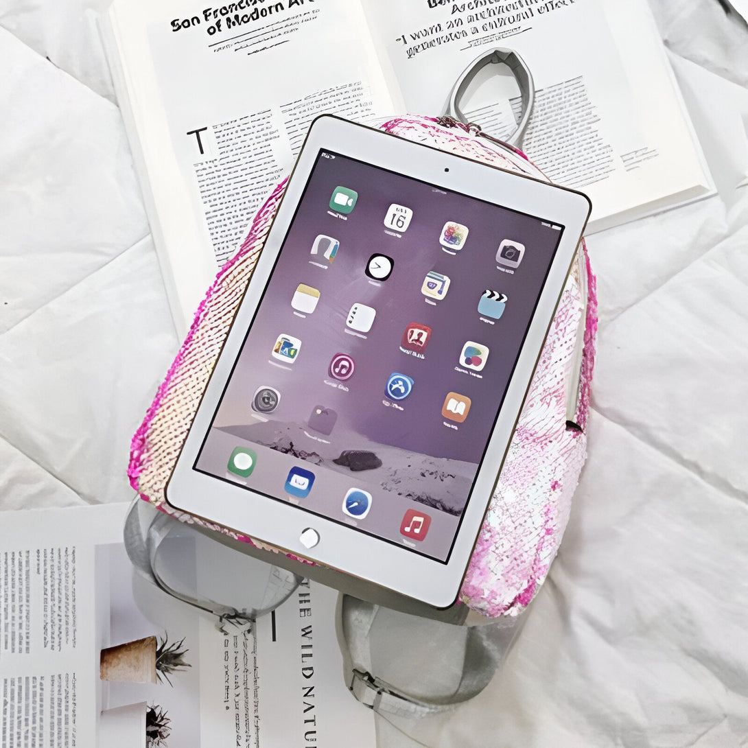 Un sac à dos rose à paillettes avec un ipad posé dessus