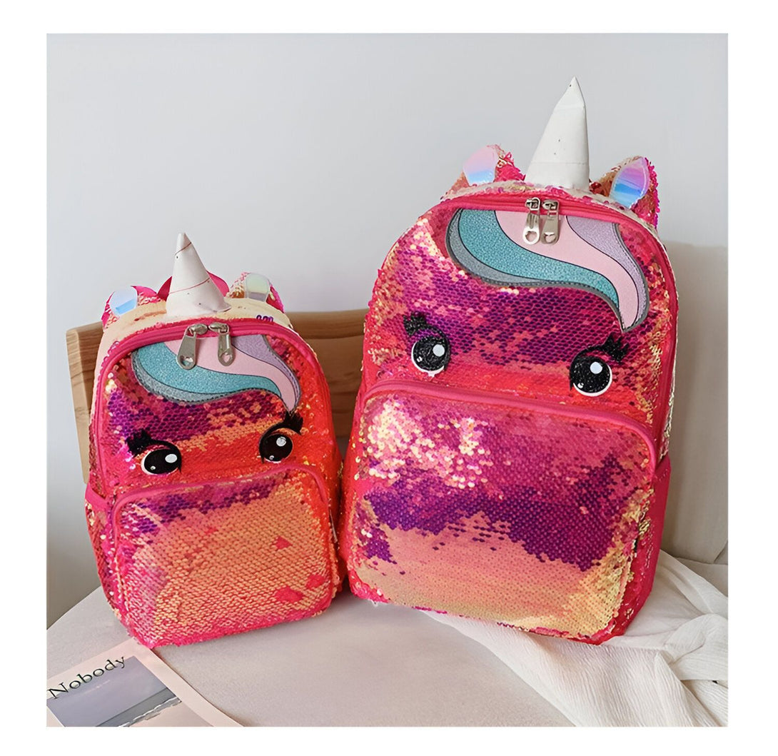 Deux sacs à dos à paillettes roses en forme de licorne sont placés sur une chaise. Les sacs à dos ont des yeux et une corne de licorne.